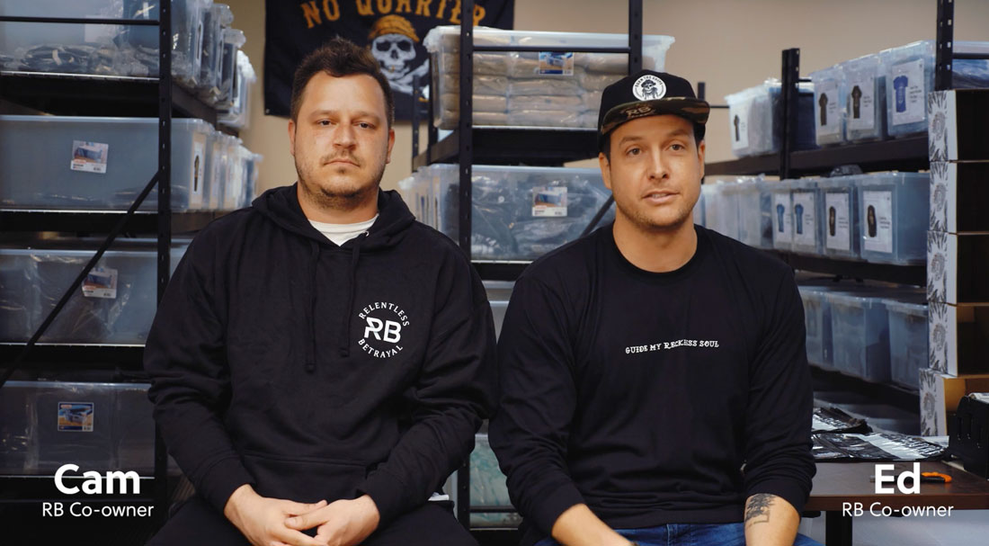 Co owners of Relentless Betrayal sitting on stools in front of their product storage area