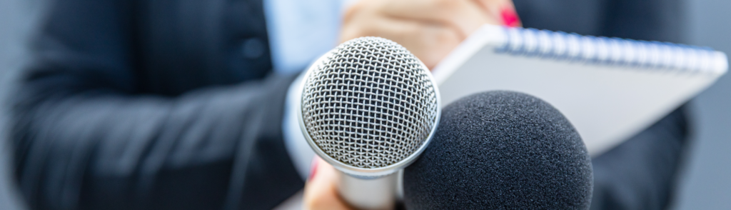 A spokesperson holds a microphone during a media interview, representing why companies partner with a PR agency